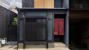 A two-story building with a dark facade, a visible entrance with a metal gate, and a small balcony with a bamboo screen. - Kanade Kiyomizu Gojo (Kyoto)