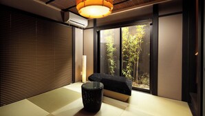 A traditional Japanese room with tatami flooring, a low table, a black cushioned bench, and a large window with bamboo outside. - Kanade Kiyomizu Gojo (Kyoto)