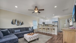 A modern living room with a grey sectional sofa, a white ottoman, and a ceiling fan.