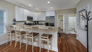 A modern kitchen with white cabinets, a stainless steel refrigerator, and a bar area with wooden chairs.