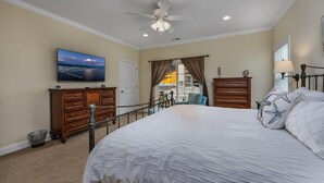 A bedroom with a large bed, a ceiling fan, a TV on the wall, and a view of the city through the window.