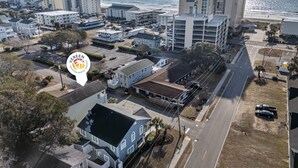 An aerial view of a coastal residential area with multiple buildings, including a prominent high-rise hotel.