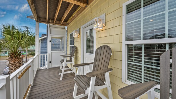 A wooden deck with Adirondack chairs, a covered porch, and a view of the ocean.