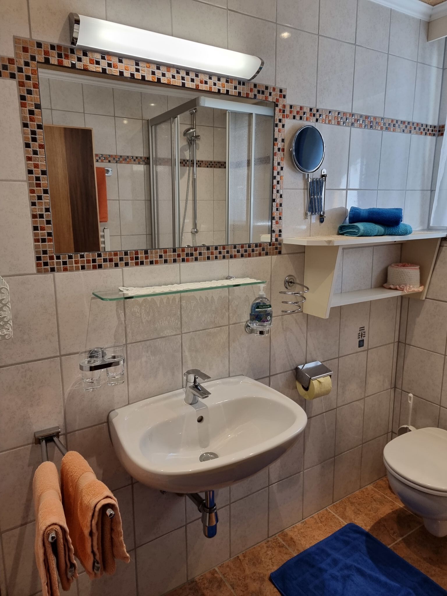 A modern bathroom with a glass shelf, a sink, a toilet, and a shower area.