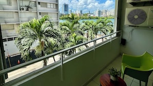 A balcony with a view of a cityscape, palm trees, and air conditioning units. - Condado Lagoon View @ Ritz Full Power Generator (San Juan)