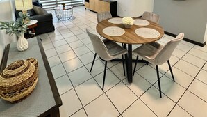 A modern living room with a dining area, featuring a round wooden table with placemats, grey upholstered chairs, and a sofa. - Condado Lagoon View @ Ritz Full Power Generator (San Juan)
