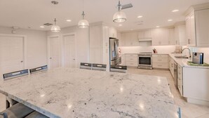 A modern kitchen with white cabinets, a large marble island, and pendant lighting. - Newly added 5-bedroom house close to Tigertail Beach!! (Marco Island)