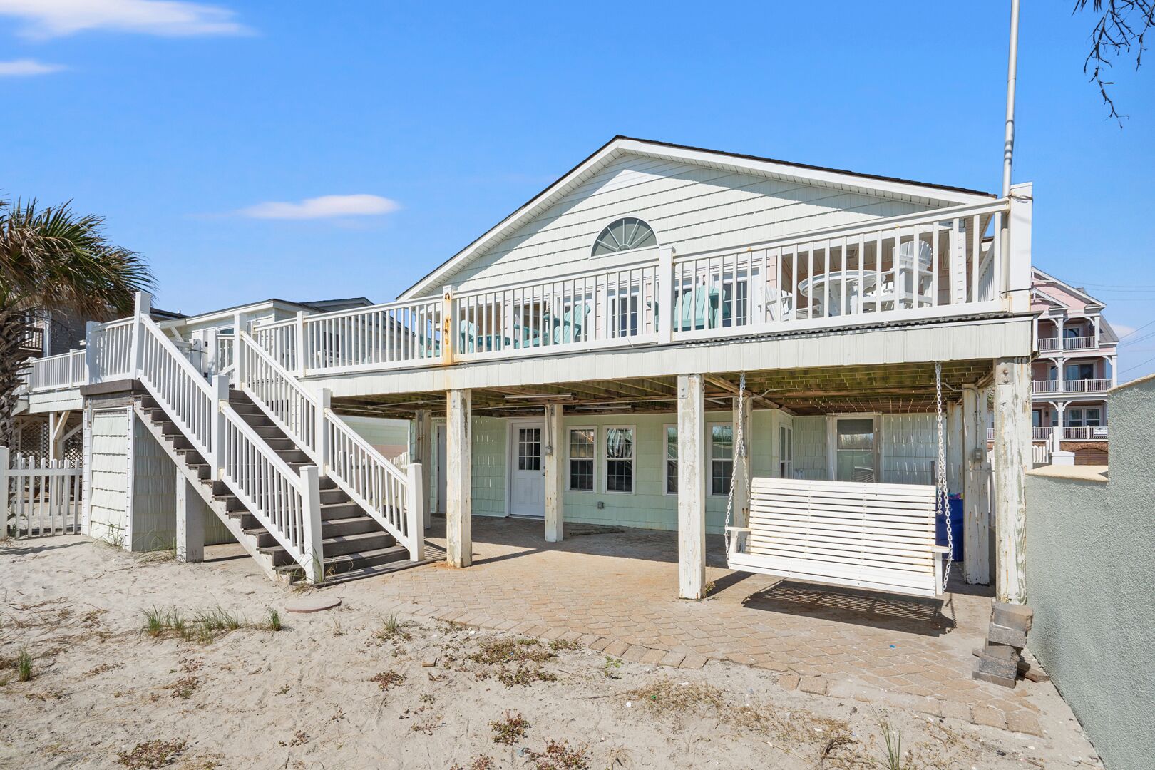 Een twee verdiepingen tellend strandhuis met een balkon, een trap en een overdekte veranda.