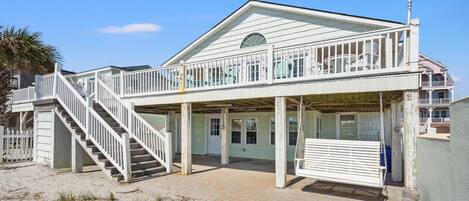Een twee verdiepingen tellend strandhuis met een balkon, een trap en een overdekte veranda.