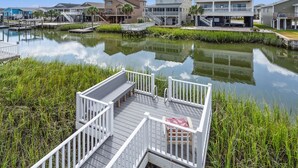 A waterfront property with a dock, a covered seating area, and a reflection of buildings in the water. - Escape to Channel Charm: Relaxing Beach Getaway in North Myrtle's Cherry Grove with Scenic Views (North Myrtle Beach)