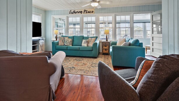 A cozy living room with teal sofas, a wooden floor, and a ceiling fan. - Escape to Channel Charm: Relaxing Beach Getaway in North Myrtle's Cherry Grove with Scenic Views (North Myrtle Beach)