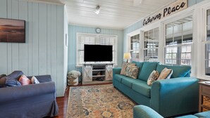 A living room with a teal sofa, a dark blue sofa, and a wooden entertainment center with a TV. - Escape to Channel Charm: Relaxing Beach Getaway in North Myrtle's Cherry Grove with Scenic Views (North Myrtle Beach)