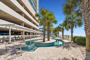 A pool area with lounge chairs, palm trees, and a building with multiple floors.
