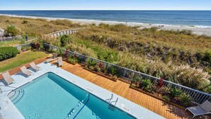 A pool area with a wooden deck, lounge chairs, and a view of the beach.