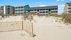 A beachfront hotel with multiple balconies, a sandy beach in the foreground, and a clear sky.