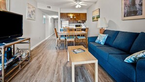 A living room with a television, a blue sofa, a coffee table, and a dining area with chairs and a table.