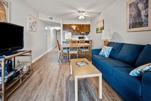 A living room with a television, a blue sofa, a coffee table, and a dining area with chairs and a table.