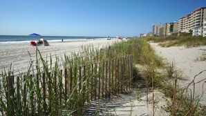 A beach with a tent and a red cooler, a wooden fence, and buildings in the background.
