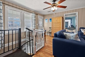A room with a wooden floor, a ceiling fan, a blue sofa, and a wooden cabinet. - Escape to Rising Tide: 8-bedroom beach retreat with private pool, hot tub, and modern amenities! (North Myrtle Beach)