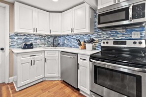 A kitchen with white cabinets, a black stove, a microwave, and a tiled backsplash. - Escape to Rising Tide: 8-bedroom beach retreat with private pool, hot tub, and modern amenities! (North Myrtle Beach)