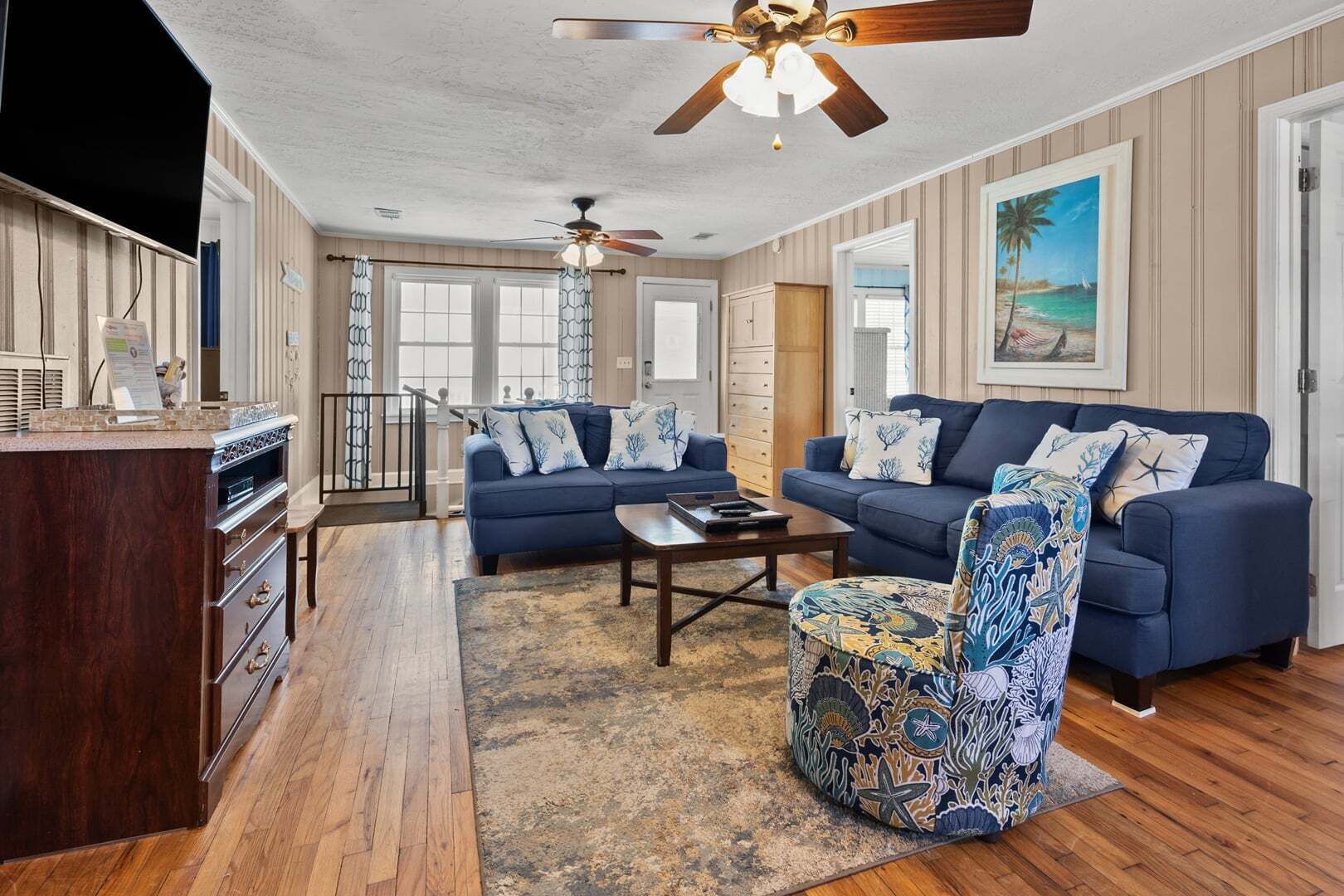 A living room with a blue sofa set, a patterned armchair, a coffee table, and a ceiling fan.