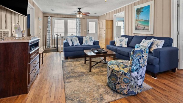 A living room with a blue sofa set, a patterned armchair, a coffee table, and a ceiling fan. - Escape to Rising Tide: 8-bedroom beach retreat with private pool, hot tub, and modern amenities! (North Myrtle Beach)