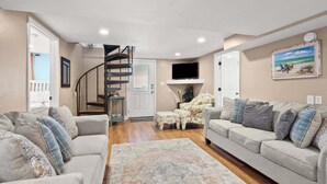 A living room with two sofas, a coffee table, a rug, a staircase, and a TV mounted on the wall. - Escape to Rising Tide: 8-bedroom beach retreat with private pool, hot tub, and modern amenities! (North Myrtle Beach)