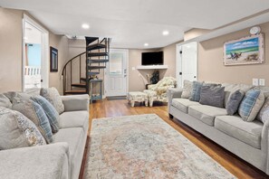 A living room with two sofas, a coffee table, a rug, a staircase, and a TV mounted on the wall.