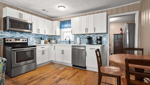 A modern kitchen with stainless steel appliances, white cabinetry, and a wooden floor. - Escape to Rising Tide: 8-bedroom beach retreat with private pool, hot tub, and modern amenities! (North Myrtle Beach)