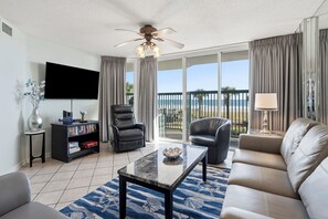 Ein Wohnzimmer mit Flachbildfernseher, Bücherregal, Ledersessel, Sofa, Couchtisch und einem Balkon mit Blick auf den Strand.