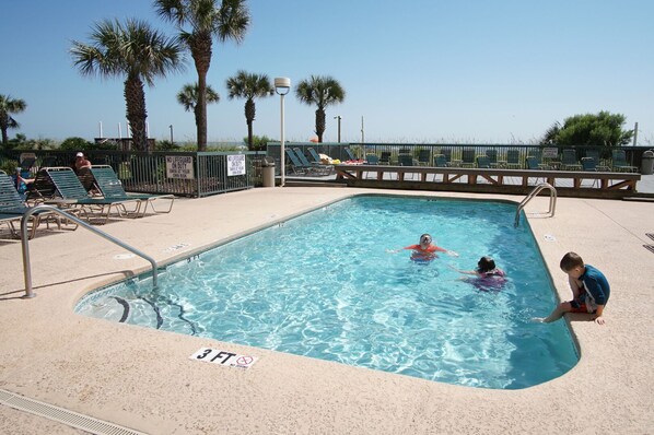 A swimming pool with a lifeguard station, lounge chairs, and palm trees in the background.