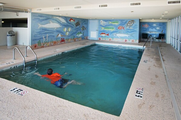 Ein Hallenbad mit einem schwimmenden Kind, umgeben von einem Wandbild mit Meereslebewesen.