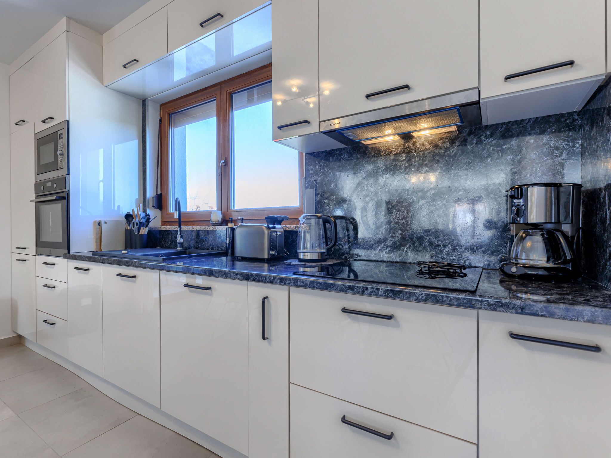 A modern kitchen with white cabinets, a black countertop, and a window above the sink.