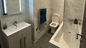 Un bany modern amb un mirall gran, un rentapeus, un vàter i una banyera.