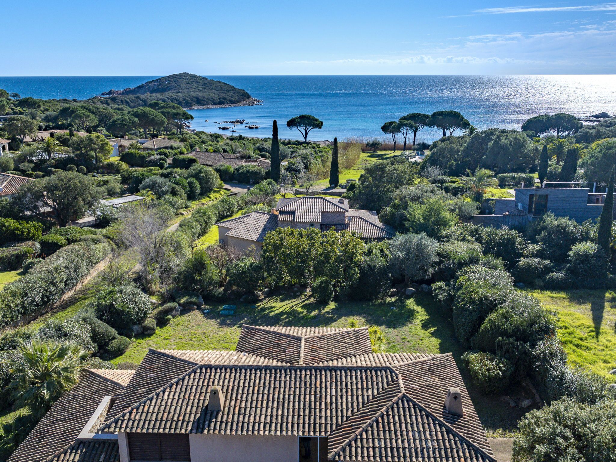 Una villa costera con techos de tejas de arcilla, rodeada de exuberante vegetación y vistas al mar.