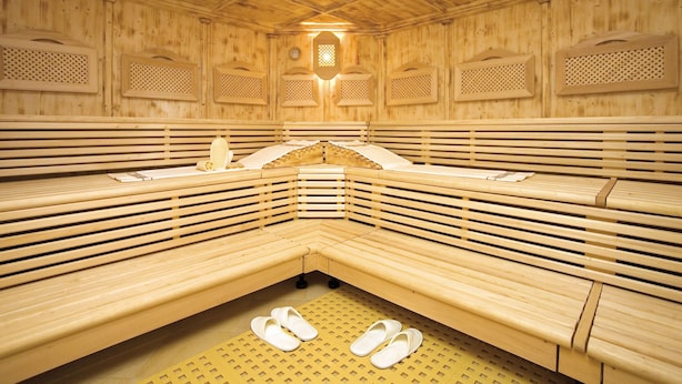 A sauna with wooden benches and benches, a bench with a towel and a bottle, and a pair of slippers on the floor. - Apartment Edith by Interhome (Imst)