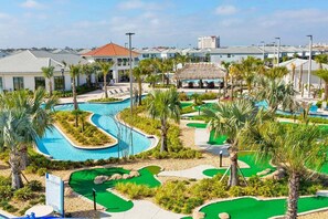 Een golfbaan met een zwembad, palmbomen en een gebouw op de achtergrond.