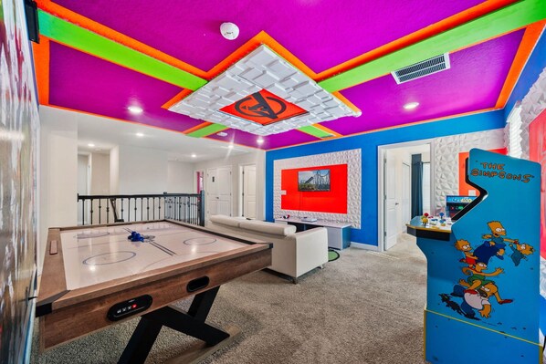 Ein helles Zimmer mit einem Kicker, einer Wandkunst in Rot und Weiß und einer Simpsons-Spieluhr.