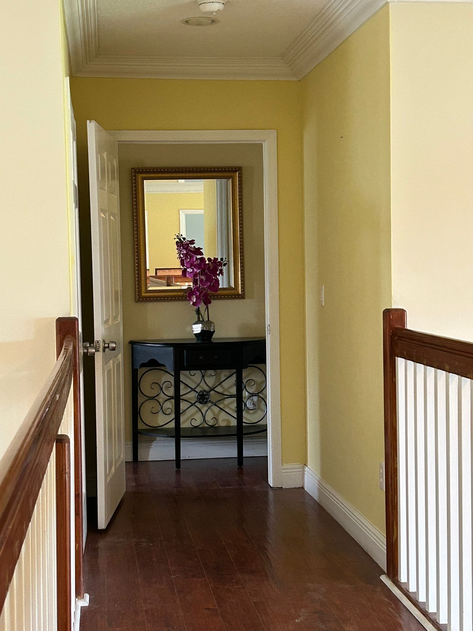 A hallway with a wooden door, a black console table with a vase of flowers, and a mirror on the wall.