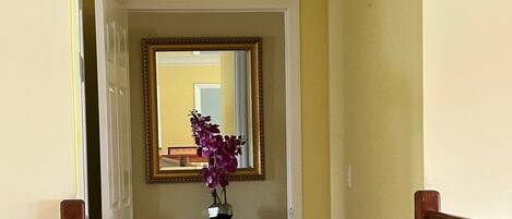 A hallway with a wooden door, a black console table with a vase of flowers, and a mirror on the wall.