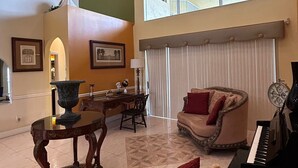 A spacious living room with a piano, a fireplace, and a large window. - Wellington Hideaway Villa a spacious 5-bedroom house close to the Polo Club (Wellington)