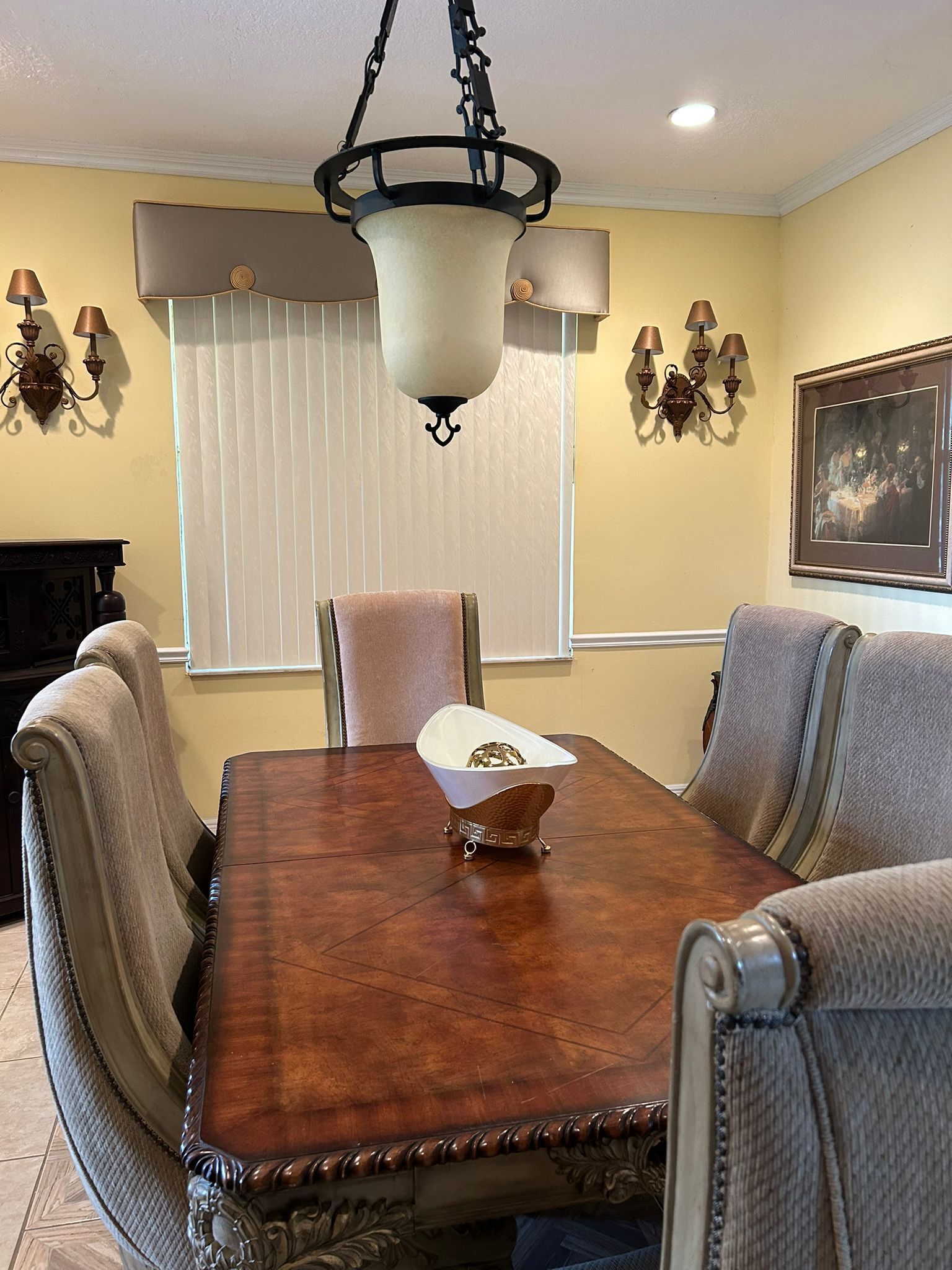 A dining room with a wooden table, upholstered chairs, a hanging light fixture, and wall sconces.