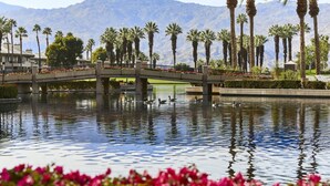A bridge over a reflective water body with palm trees and mountains in the background. - Marriott Desert Spring Villas- available march 2-9 only (palm desert)