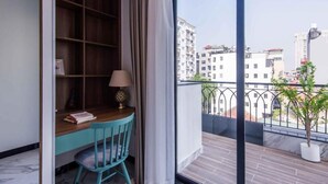 Un balcon donnant sur des immeubles, un bureau en bois avec une lampe et une chaise.