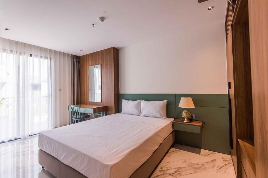 Une chambre d’hôtel moderne dotée d’un grand lit, d’un bureau avec une chaise, d’une table de chevet avec une lampe et offrant une vue sur l’extérieur grâce à de grandes fenêtres.