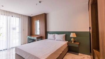 Une chambre d’hôtel moderne dotée d’un grand lit, d’un bureau avec une chaise, d’une table de chevet avec une lampe et offrant une vue sur l’extérieur grâce à de grandes fenêtres.