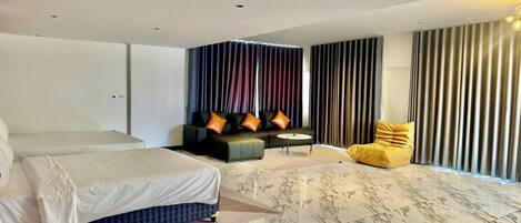 A modern hotel room with a large bed, a sofa, a yellow bean bag, and a small table.