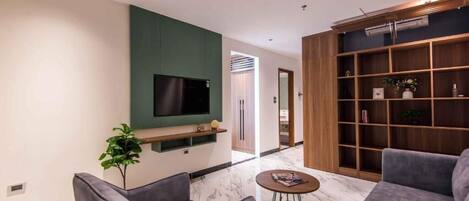 Un salon moderne avec un téléviseur à écran plat fixé sur un mur vert, une bibliothèque en bois et deux canapés gris.