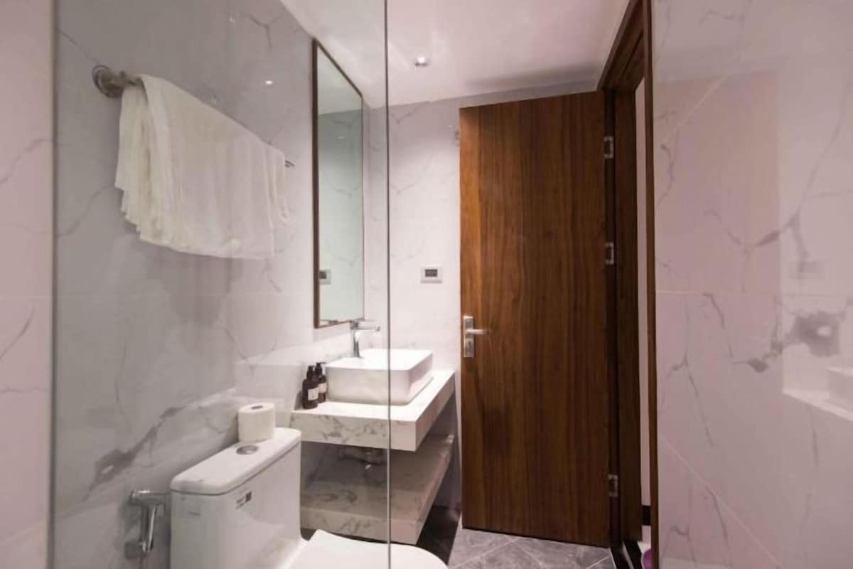 Un baño moderno con cabina de ducha de vidrio, inodoro blanco, tocador con espejo y puerta de madera.