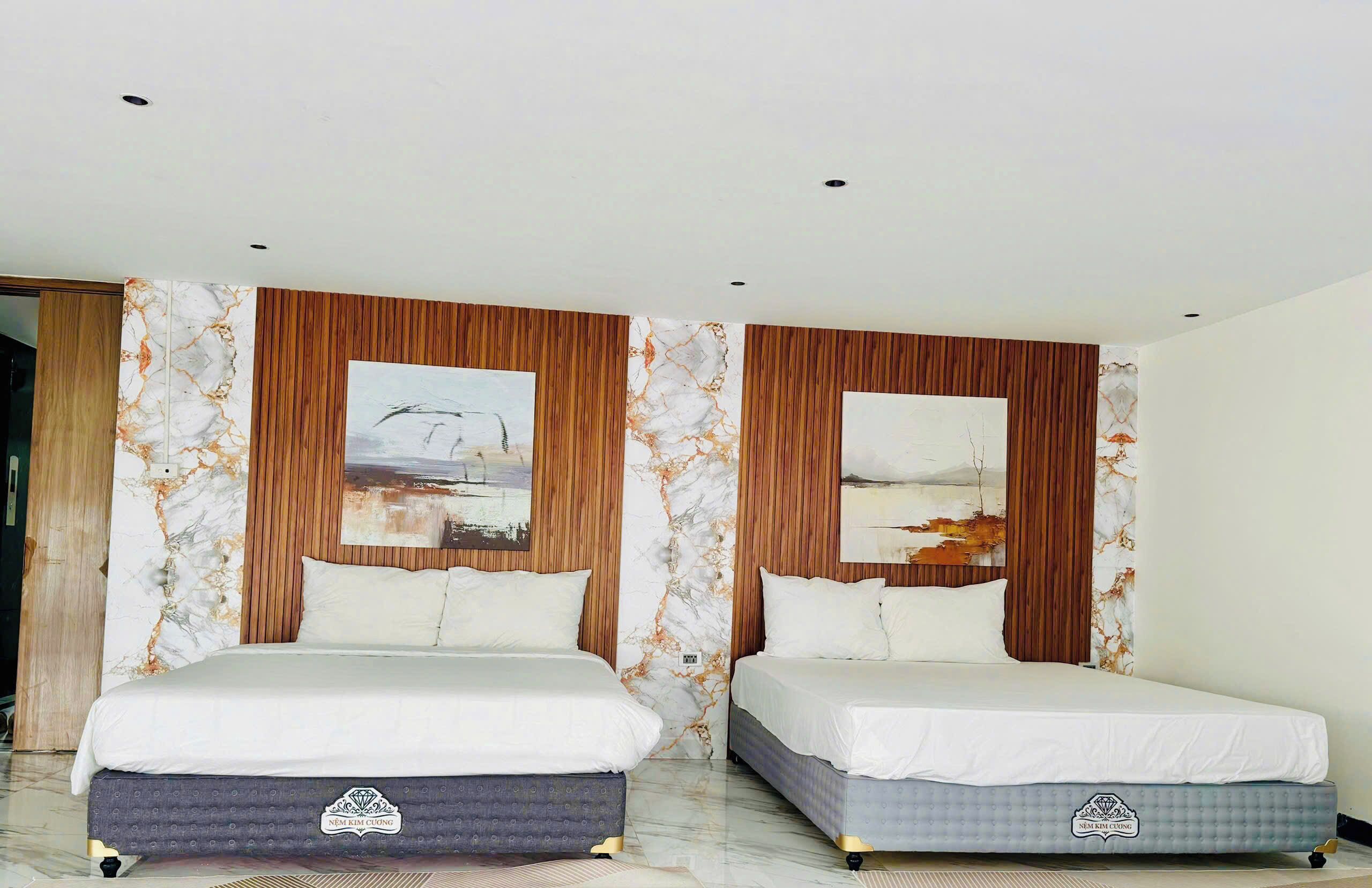 Habitación de hotel con dos camas, paneles de madera, diseños en la pared que imitan mármol y obras de arte.